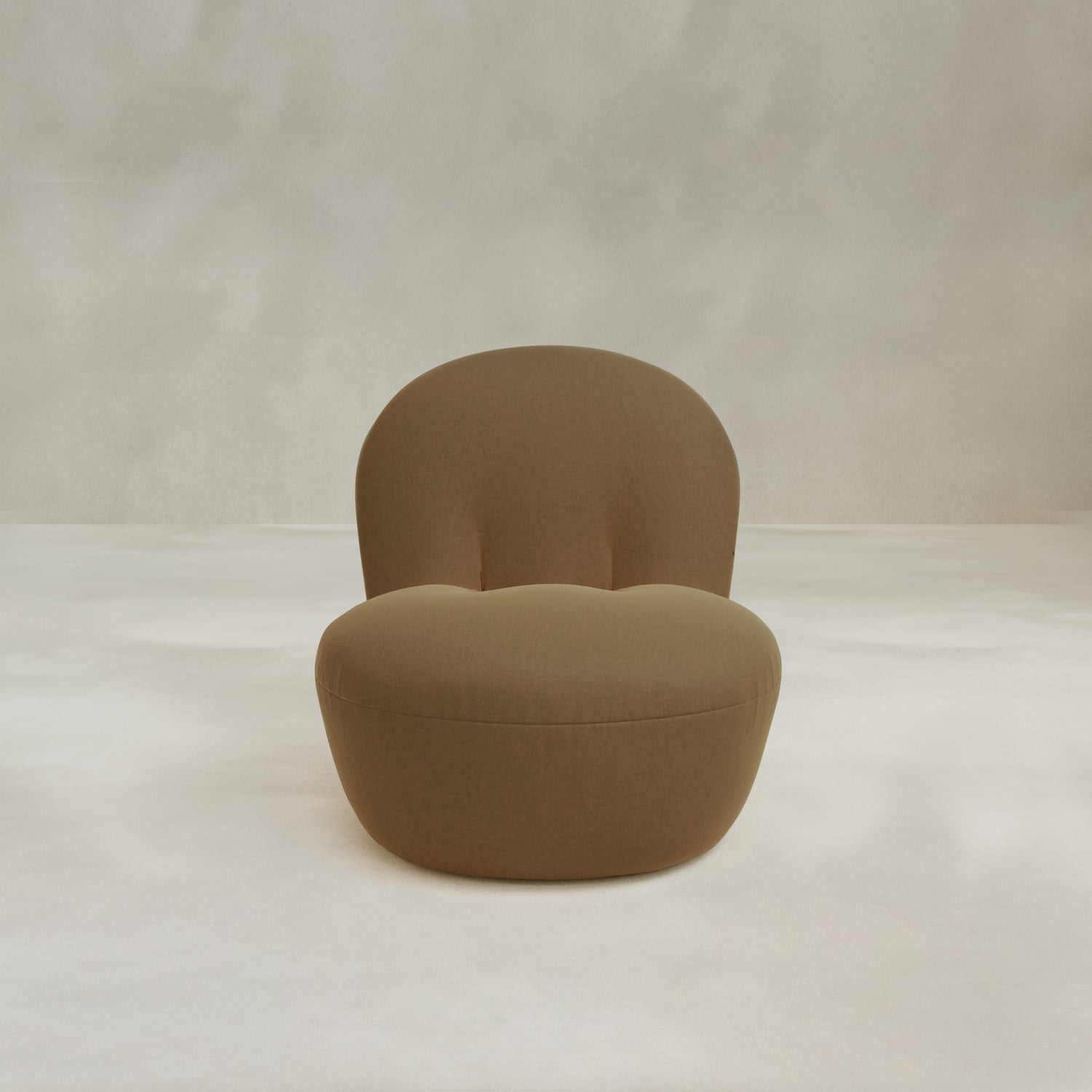 The Colette Chair, a modern brown upholstered lounge chair with a rounded backrest and seat, adds contemporary flair and rich texture to any space against a light, neutral backdrop.