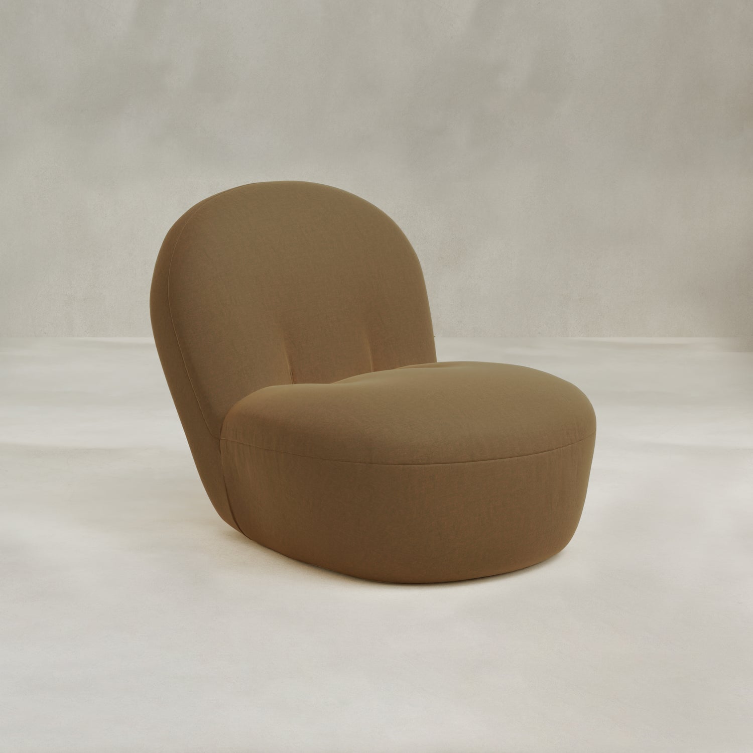 The Colette Chair, a modern armless lounge chair with a rounded back and light brown upholstery, adds contemporary flair and rich texture when placed against a light, neutral background.