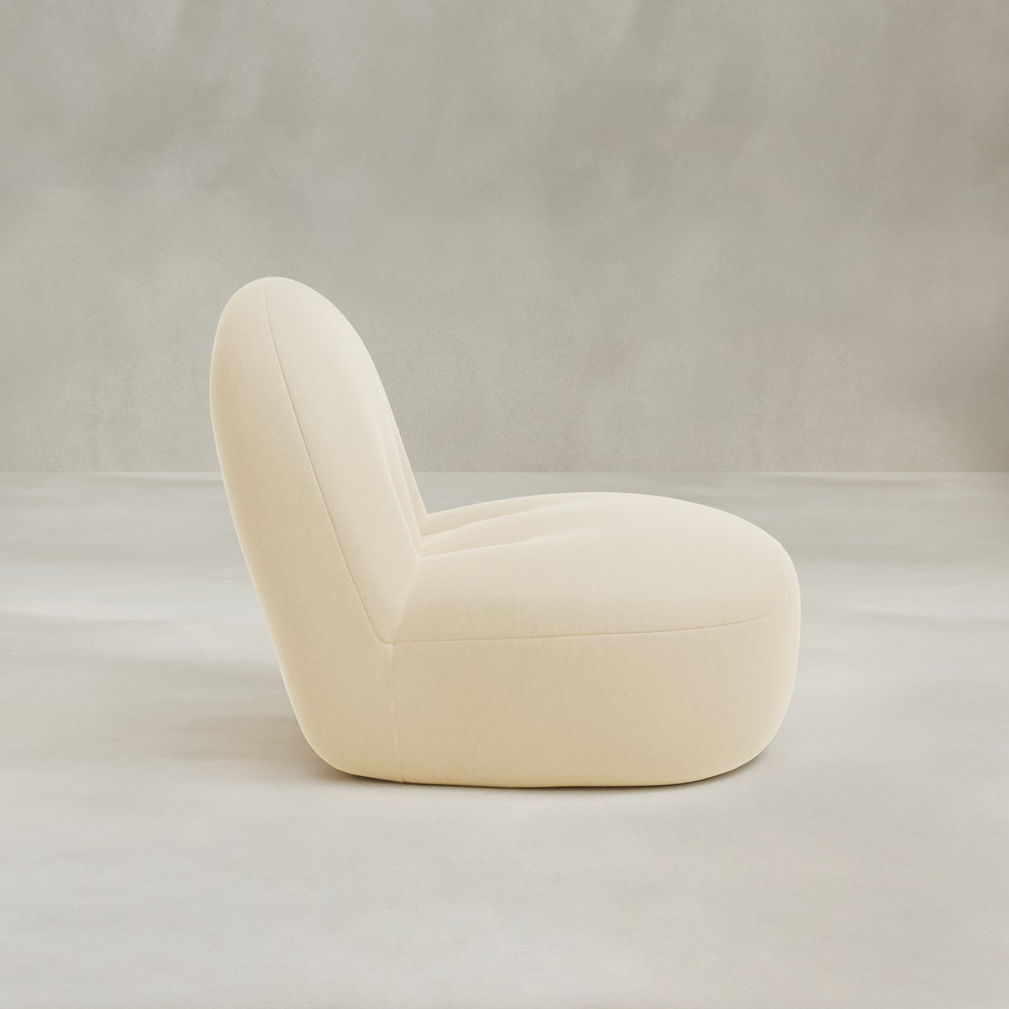 The Colette Chair is a modern, minimalist cream-colored lounge chair with plush cushions and a rounded, low-profile design, shown in side view against a neutral light gray background.