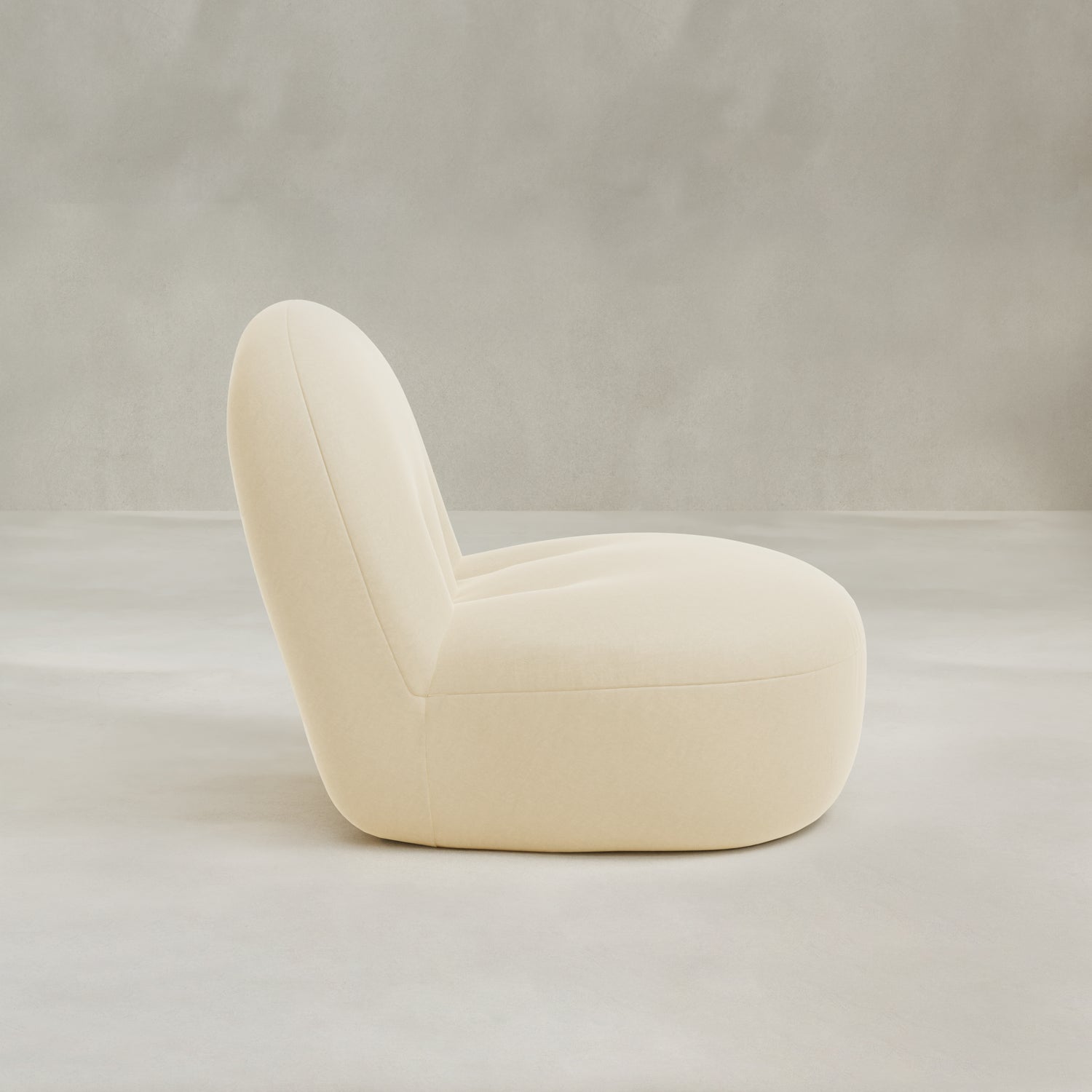 The Colette Chair is a modern, minimalist cream-colored lounge chair with plush cushions and a rounded, low-profile design, shown in side view against a neutral light gray background.