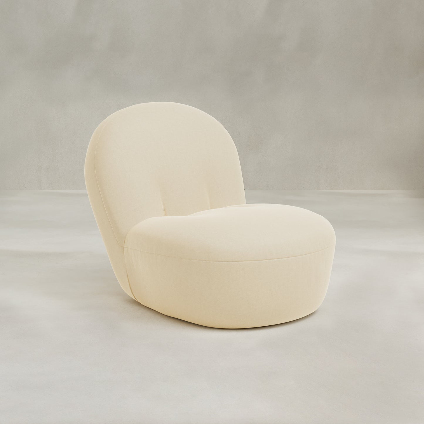The Colette Chair is a modern, beige upholstered lounge chair with a rounded backrest and seat. Its seamless, minimalist design and rich texture offer contemporary flair on a neutral light gray background, with no visible legs or armrests.
