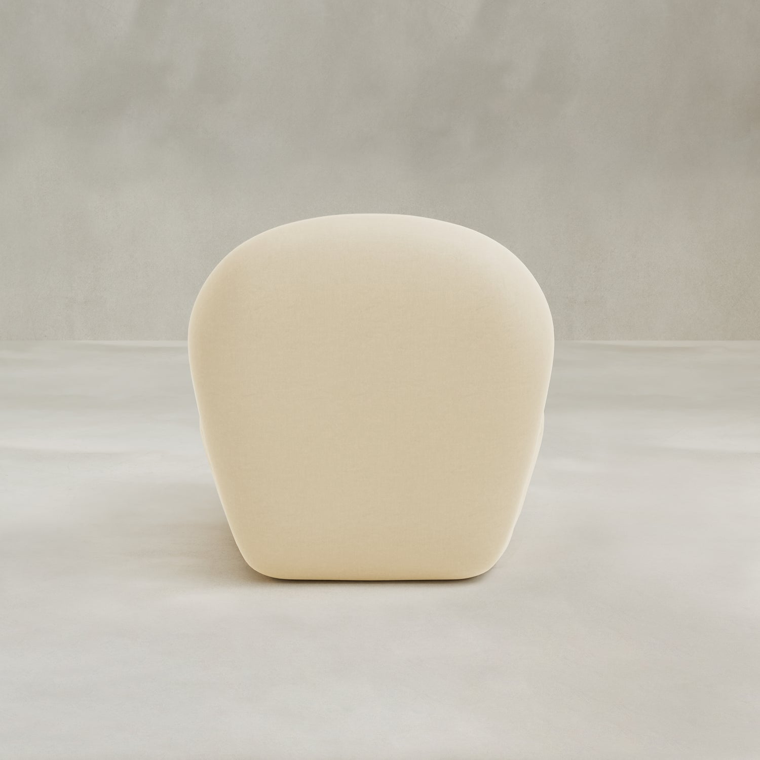 The Colette Chair, a modern minimalist piece with a rounded backrest and smooth beige upholstery, adds contemporary flair. Shown from the back against a seamless light grey background.