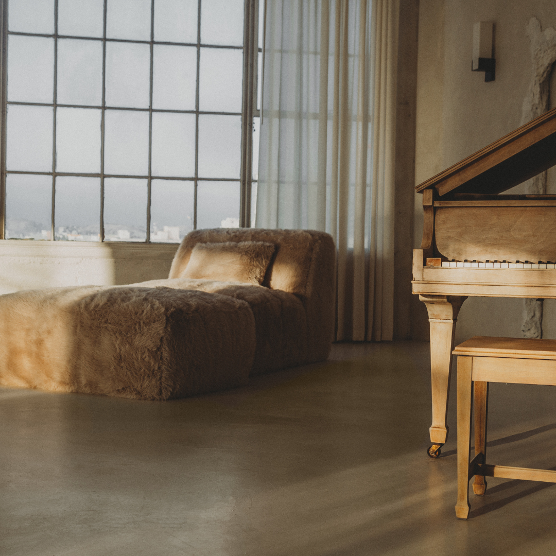 The Yeti Chaise Lounge, upholstered in soft beige faux fur, adds luxurious comfort and style to a minimalist room with light walls and flooring.