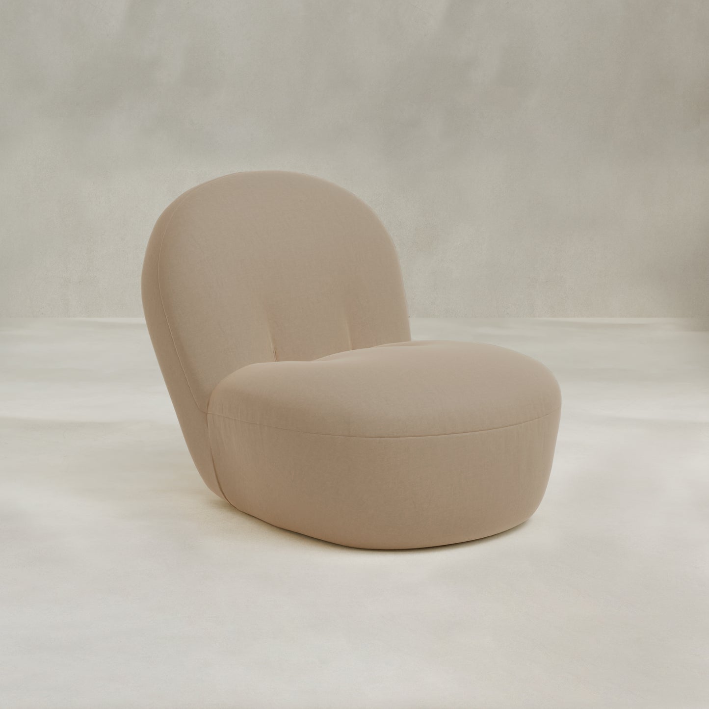 The Colette Chair is a minimalist beige lounge chair with plush cushions, a rounded seat, and curved backrest, set against a neutral textured background for contemporary flair.