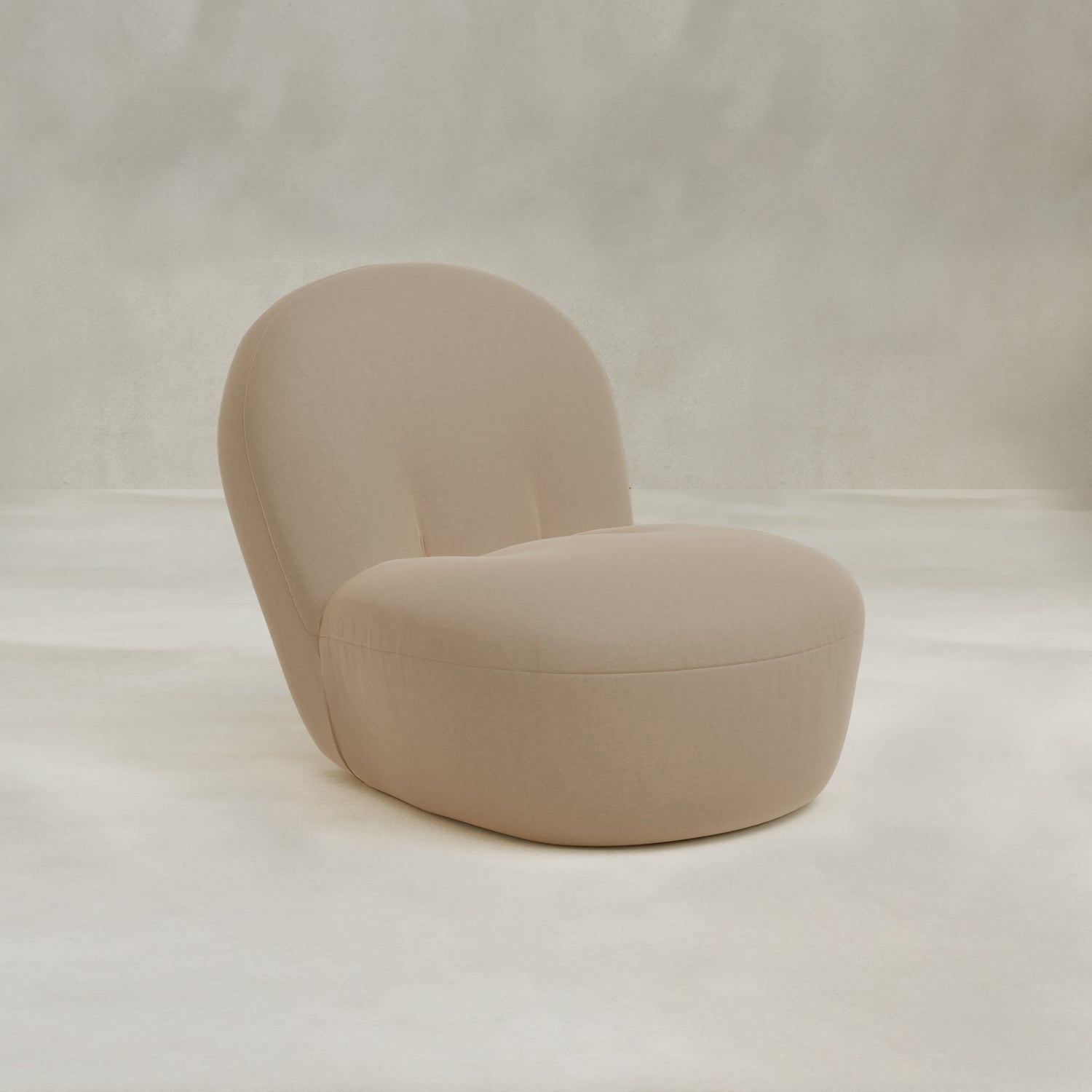 The Colette Chair is a minimalist beige lounge chair with plush cushions, a rounded seat, and curved backrest, set against a neutral textured background for contemporary flair.