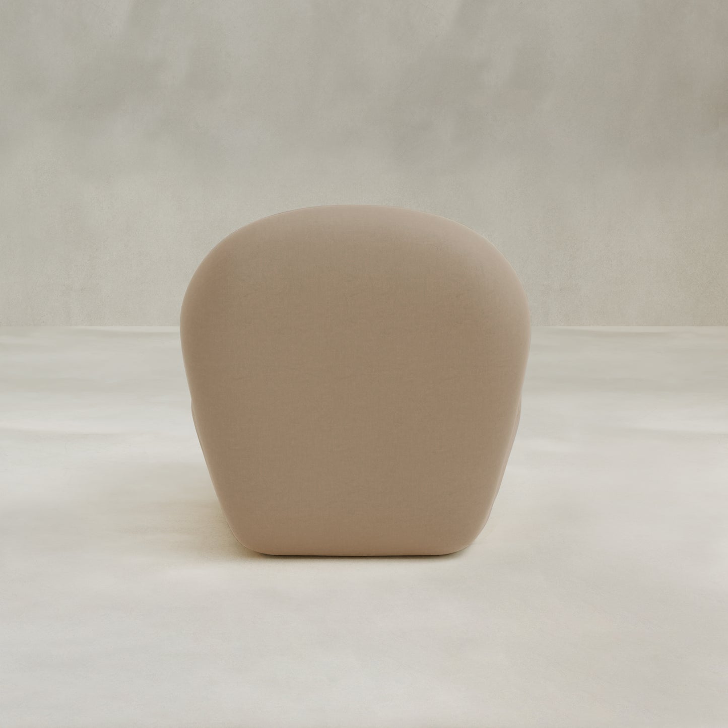 The Colette Chair, a beige, rounded modern seat with plush cushions and hidden legs, rests on a light neutral floor against a softly textured wall, bringing contemporary flair to the space.