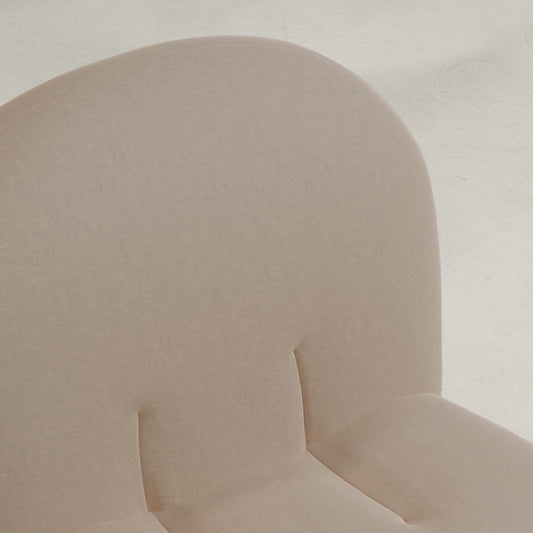 A close-up of the Colette Chair showcases its modern design, light beige upholstery, rounded backrest, and rich texture with soft, smooth fabric on a light-colored surface.
