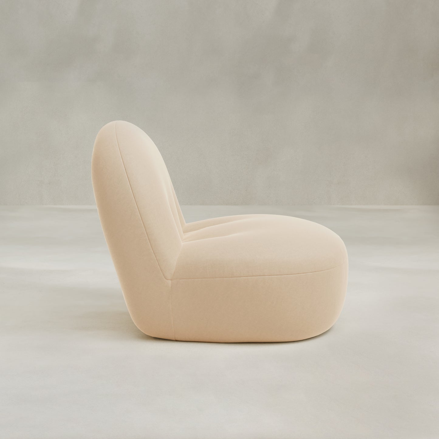 The Colette Chair is a modern, low-profile lounge chair with plush cushions, soft rounded edges, and light beige upholstery, shown in profile view against a neutral gray background.