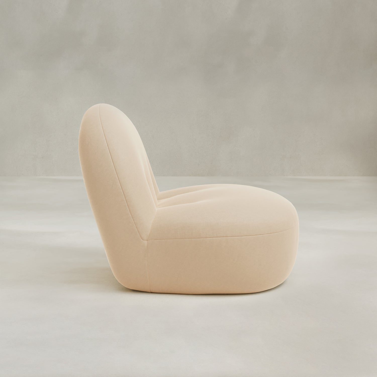 The Colette Chair is a modern, low-profile lounge chair with plush cushions, soft rounded edges, and light beige upholstery, shown in profile view against a neutral gray background.