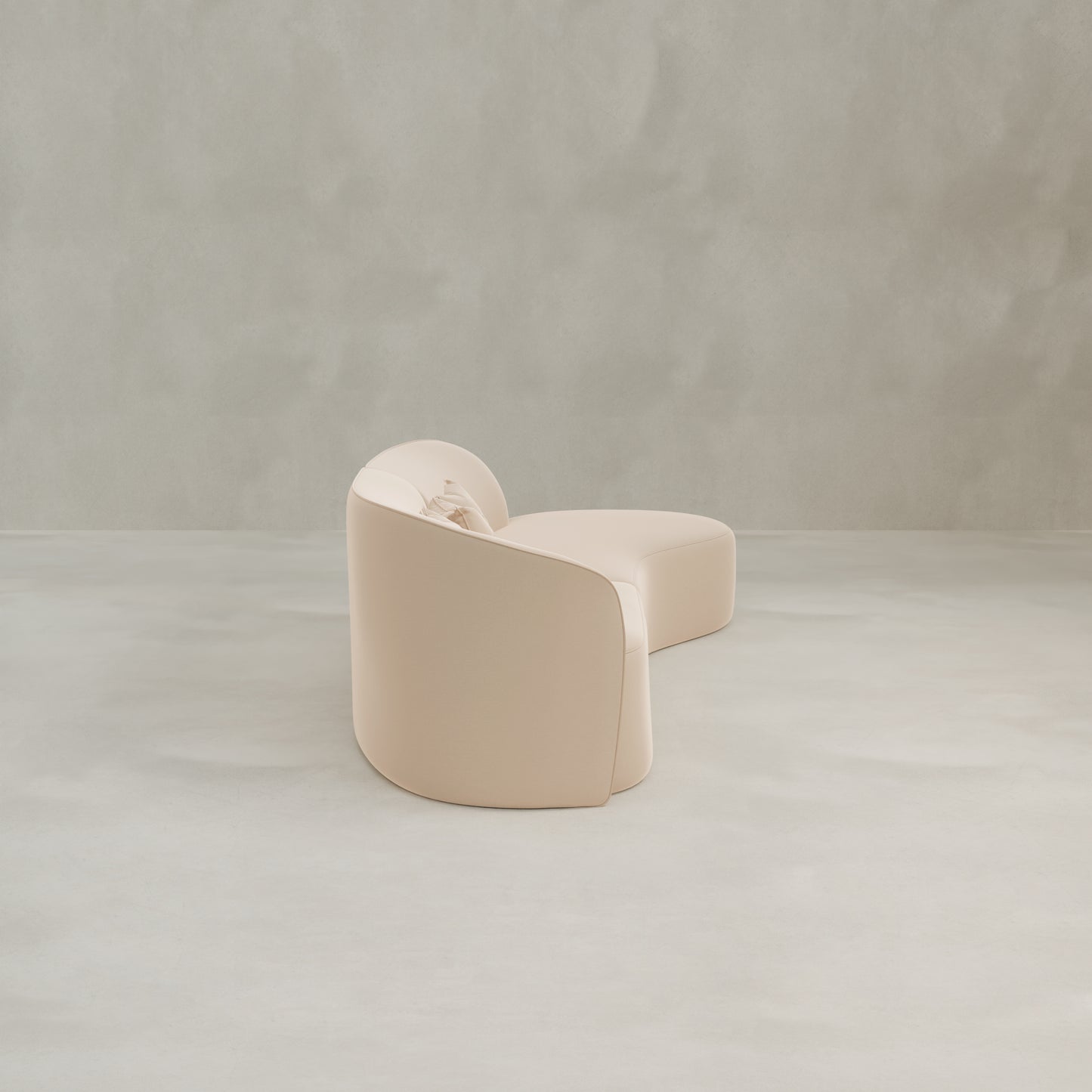 The Marlow Curved Modular Three Seater Sofa, featuring luxurious beige upholstery and soft, rounded edges, sits on a smooth light grey floor against a plain, textured grey wall.