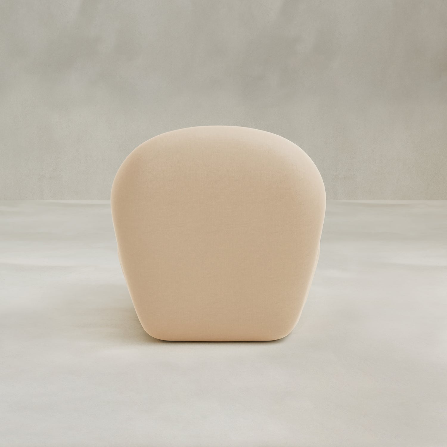 The Colette Chair is a beige, rounded armchair with plush cushions, shown from the back against a neutral textured background. Its minimalist design features smooth curves and a simple, modern look.