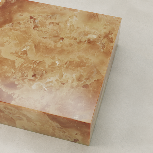 A large, rectangular Ambeline Onyx Coffee Table XL features polished brownish-orange marble with rust, white, and tan veining, sitting on a light gray surface and radiating refined organic elegance.