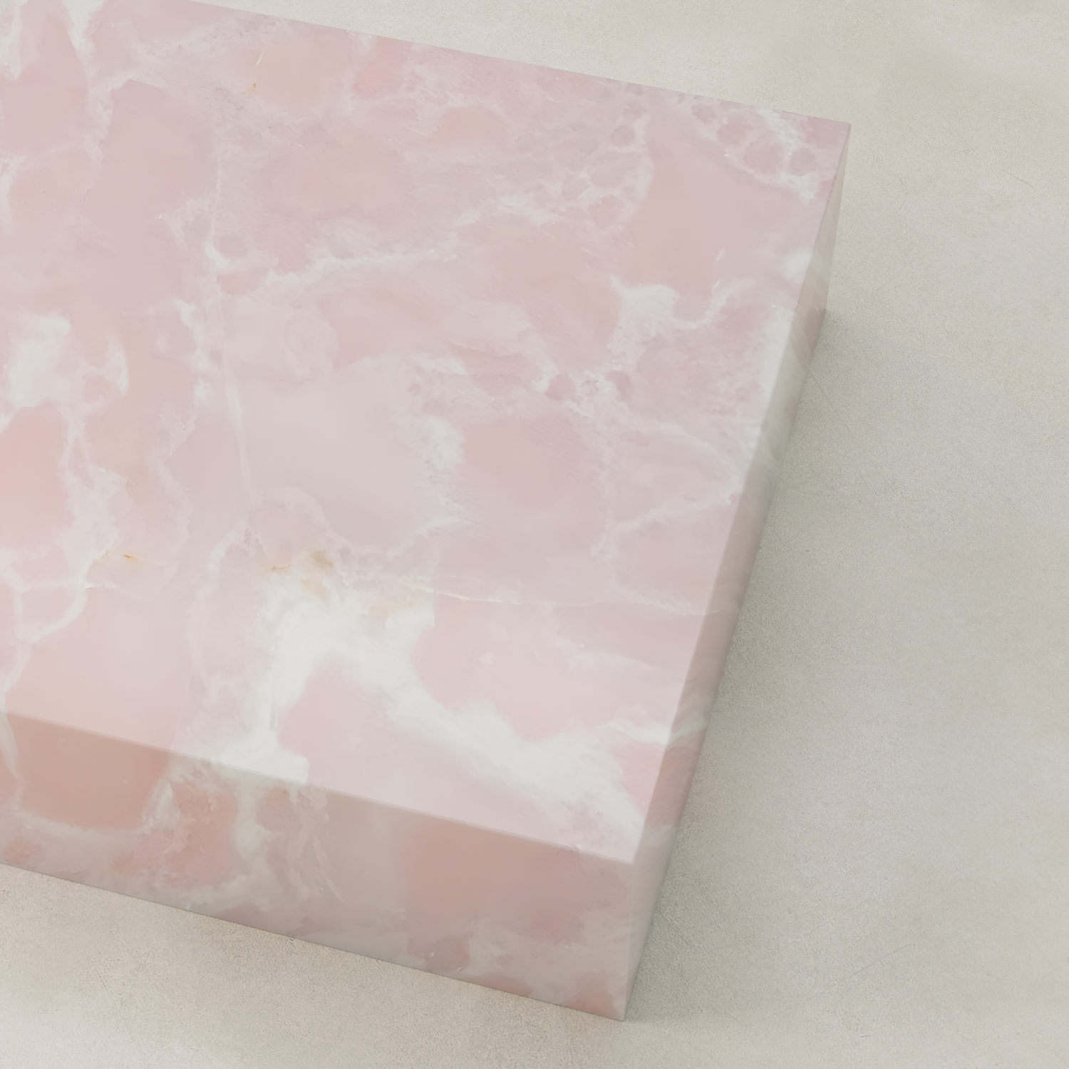 The Cora Onyx Coffee Table XL is a large rectangular piece featuring glossy pink onyx with white veining, a soft cloudy texture, and a polished finish. It sits elegantly on a light-colored, smooth surface.
