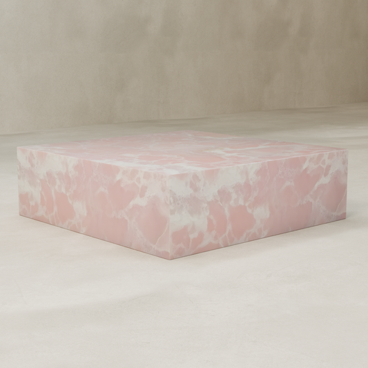The Cora Onyx Coffee Table XL, a large rectangular piece with a pink and white marbled finish, sits on a smooth, light-colored floor against a neutral beige wall.