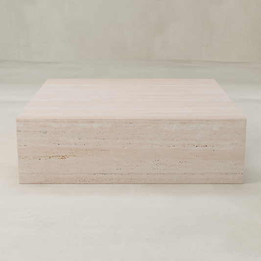The Alessia Coffee Table XL, a rectangular light beige travertine piece with modern lines, stands on a matching floor against a neutral wall, forming a striking statement in the room.