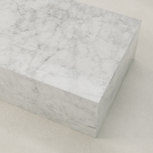 The Griselle Marble Coffee Table features a large rectangular block of smooth white marble with gray veining, resting on a light, textured surface for an elegant, minimalist look.