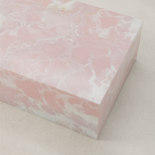 A rectangular block with a smooth surface shows a pink and white marbled pattern, resembling the Cora Onyx Coffee Table, and is placed on a light-colored background.