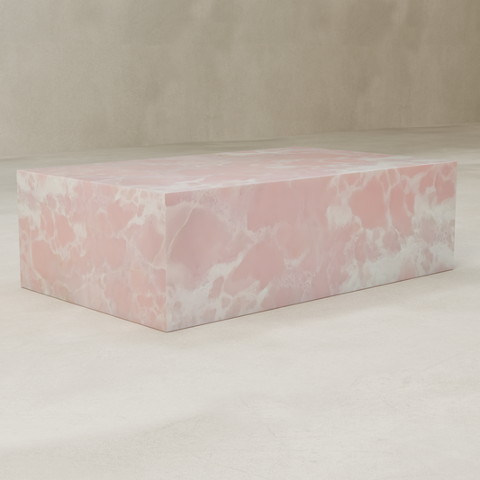 The Cora Onyx Coffee Table, featuring a smooth, glossy pink and white marble-like surface, stands on a light textured floor against a beige wall.