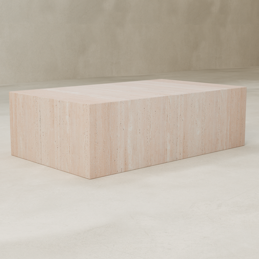 The Alessia Coffee Table, a rectangular beige travertine piece with a smooth, minimalist design, sits on a light polished floor against a neutral wall.