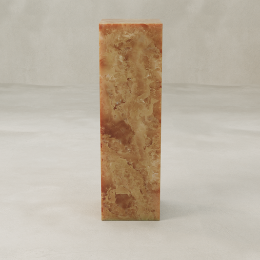 The Ambeline Onyx Tall Tower Plinth, crafted from polished brown and amber marble, exudes organic elegance as it stands on a smooth, light-colored surface against a neutral background.