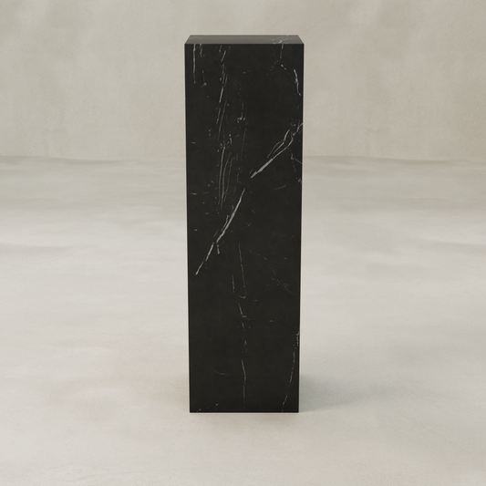 The Obscara Plinth - Tall Tower is a tall, rectangular black marble plinth with subtle white veining, displayed on a smooth, light surface against a neutral background for a look of timeless sophistication.