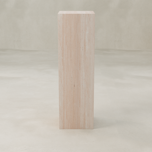 The Alessia Tall Tower Plinth, a rectangular piece crafted from light-colored travertine, stands on a neutral floor with a matching background and features subtle natural vertical lines and textures for a modern look.