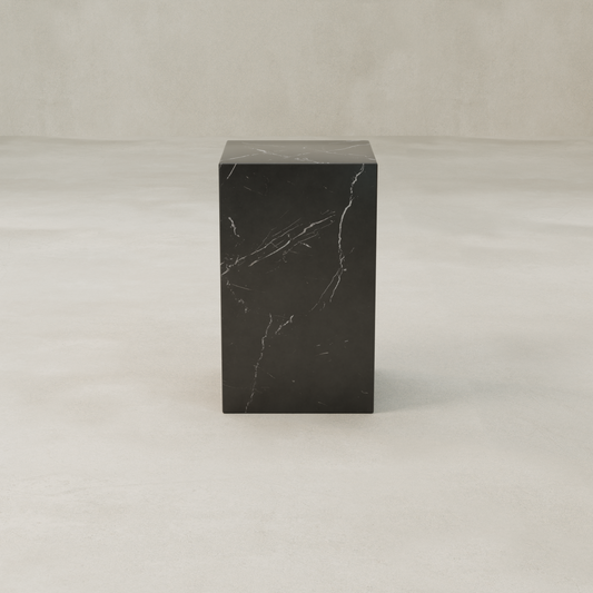 The Obscara Plinth - Tall, a tall rectangular black marble pedestal with subtle white veining, adds timeless sophistication as it stands on a smooth light beige surface against a matching neutral background.