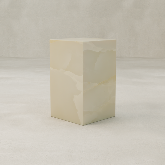 The Lunelle Onyx Plinth - Tall, a rectangular piece in light beige with subtle marbled patterns, stands as a sculptural focal point on a pale textured surface against a neutral background.