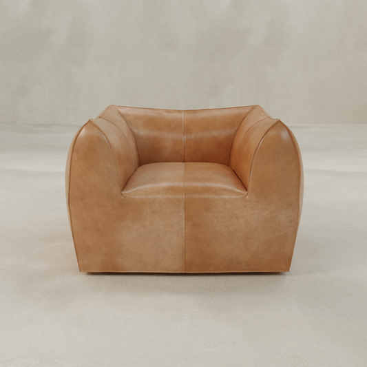 The Bambon Armchair features a modern, boxy design with vintage leather upholstery, wide rounded arms, and a low back, showcased against a light minimalist background.
