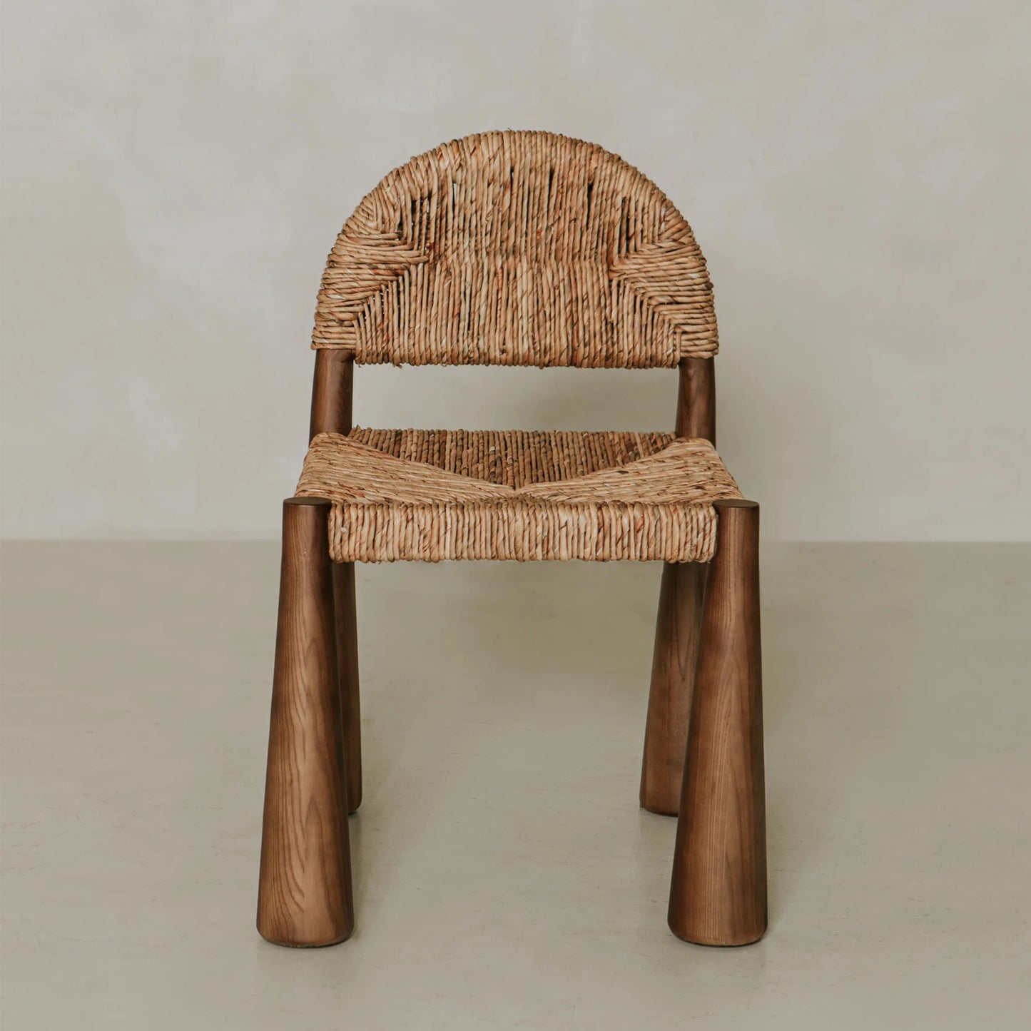 The Renè + Bardo Dining Set features a modern chair with a woven rattan seat and backrest, cylindrical wooden legs, and is displayed against a neutral background.