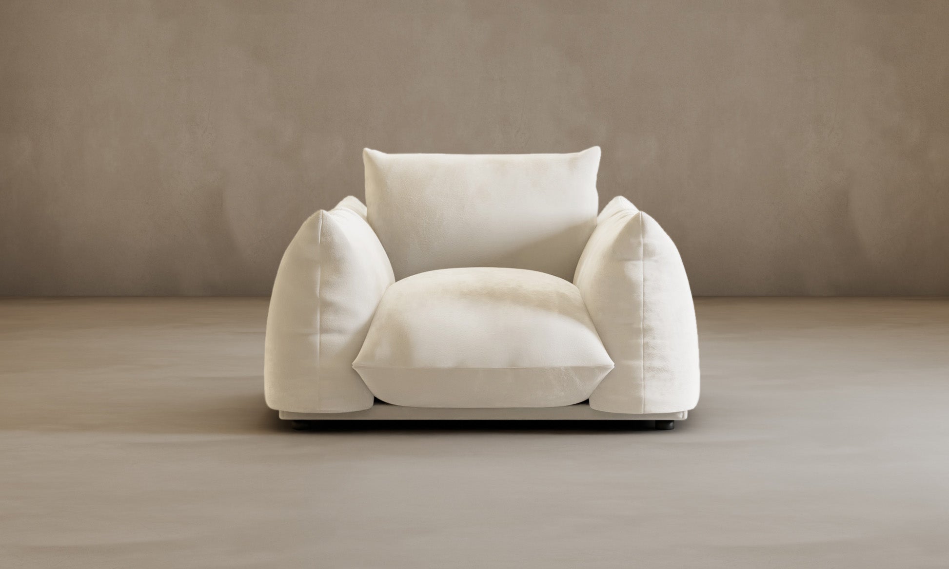 The large Calypso Arm Chair in dark brown features wide, plush cushions and sits on a light beige floor with a plain beige wall backdrop, creating an inviting and cozy look.