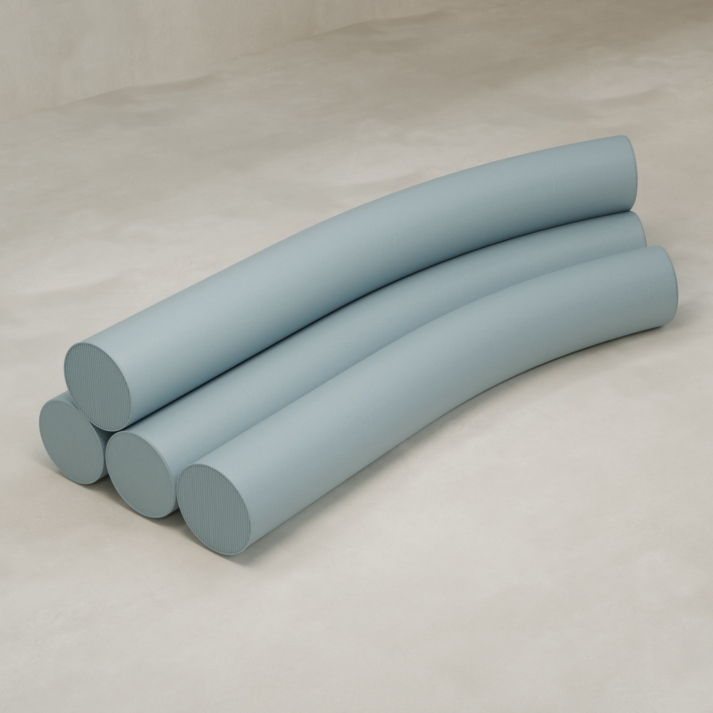 Four long, light blue cushions are stacked in two layers on a beige surface, each slightly arched and aligned side by side, resembling the soft forms of the Cylindra Sofa.