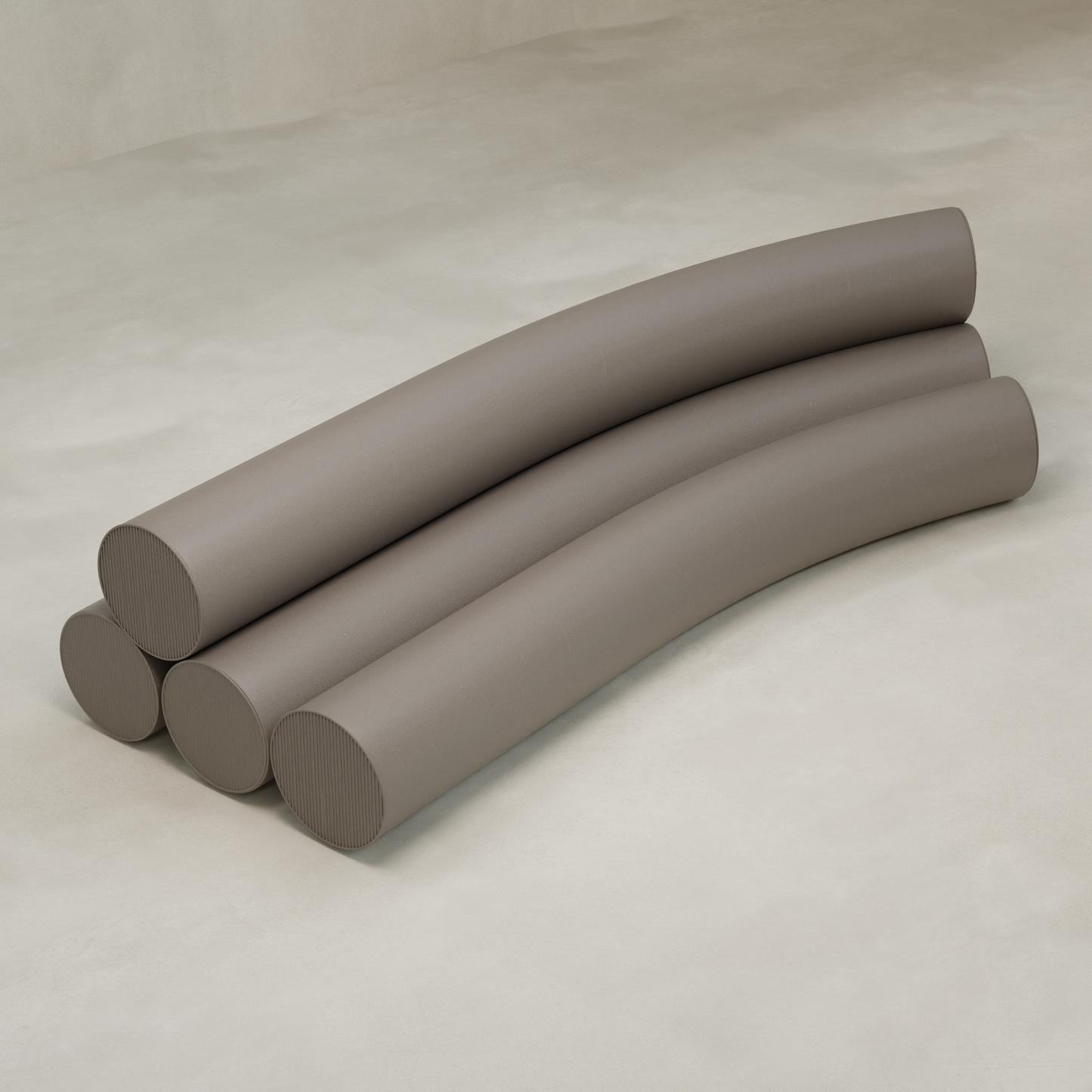 Four large, smooth, taupe cylinders are stacked on a light textured surface. The top two curve gently, forming the arching silhouette of the Cylindra Sofa over the two below.