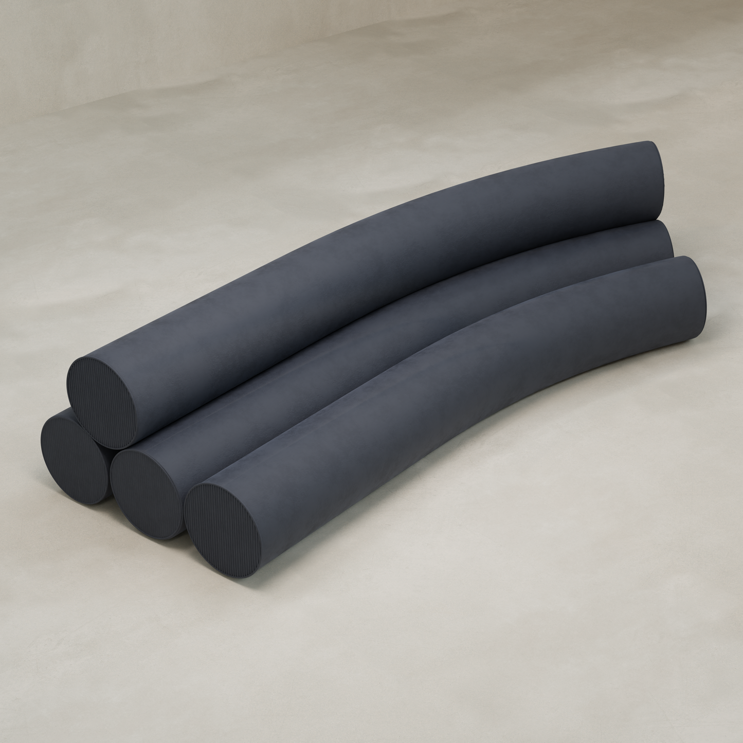 Four long, cylindrical dark gray cushions are stacked in a staggered horizontal formation on a light surface, creating the Cylindra Sofa—a modern piece with minimalist and neotenic design elements.