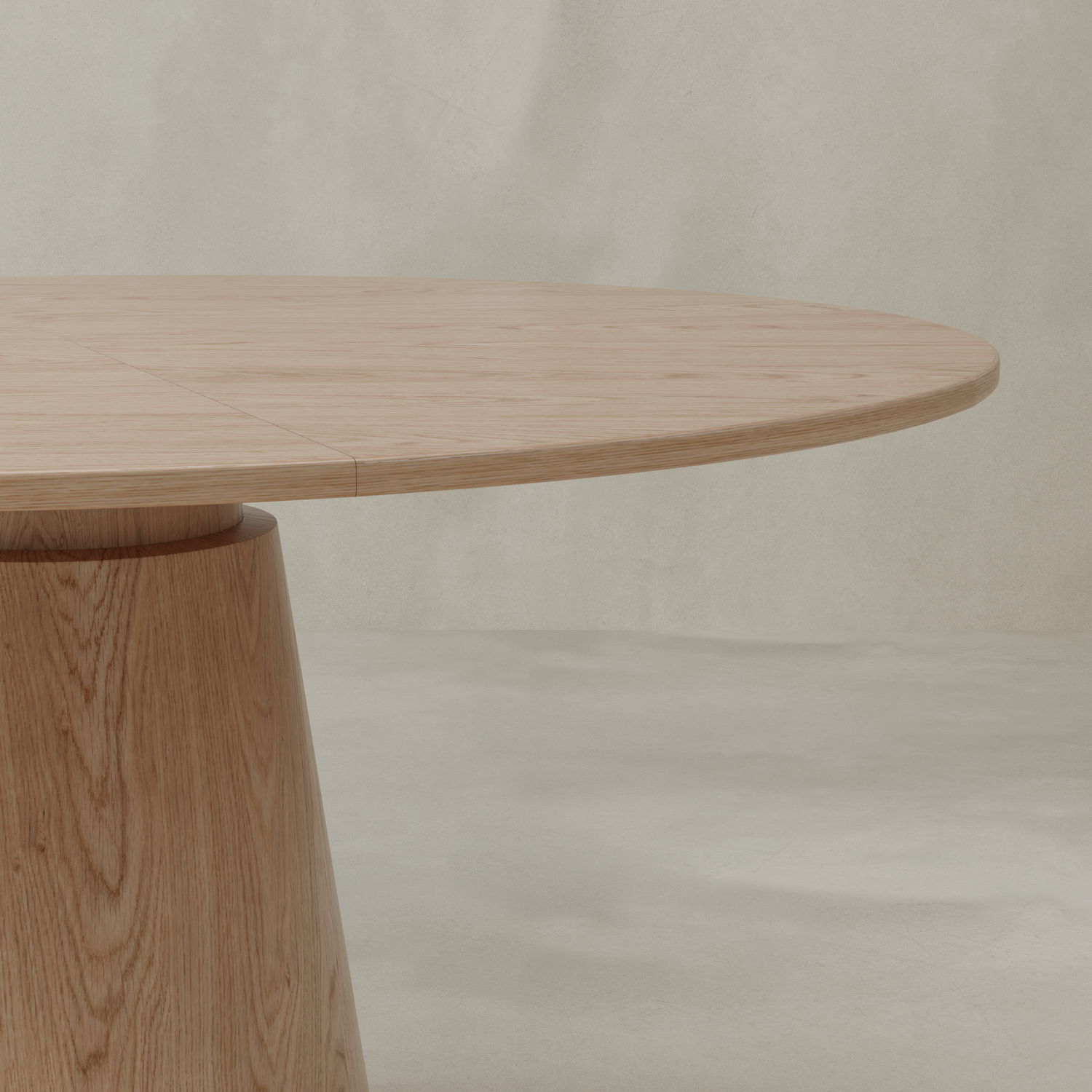 A close-up view of the Harlow Dining Table, featuring a smooth, natural wood finish and a thick, cylindrical pedestal base, set against a plain light beige wall and floor.