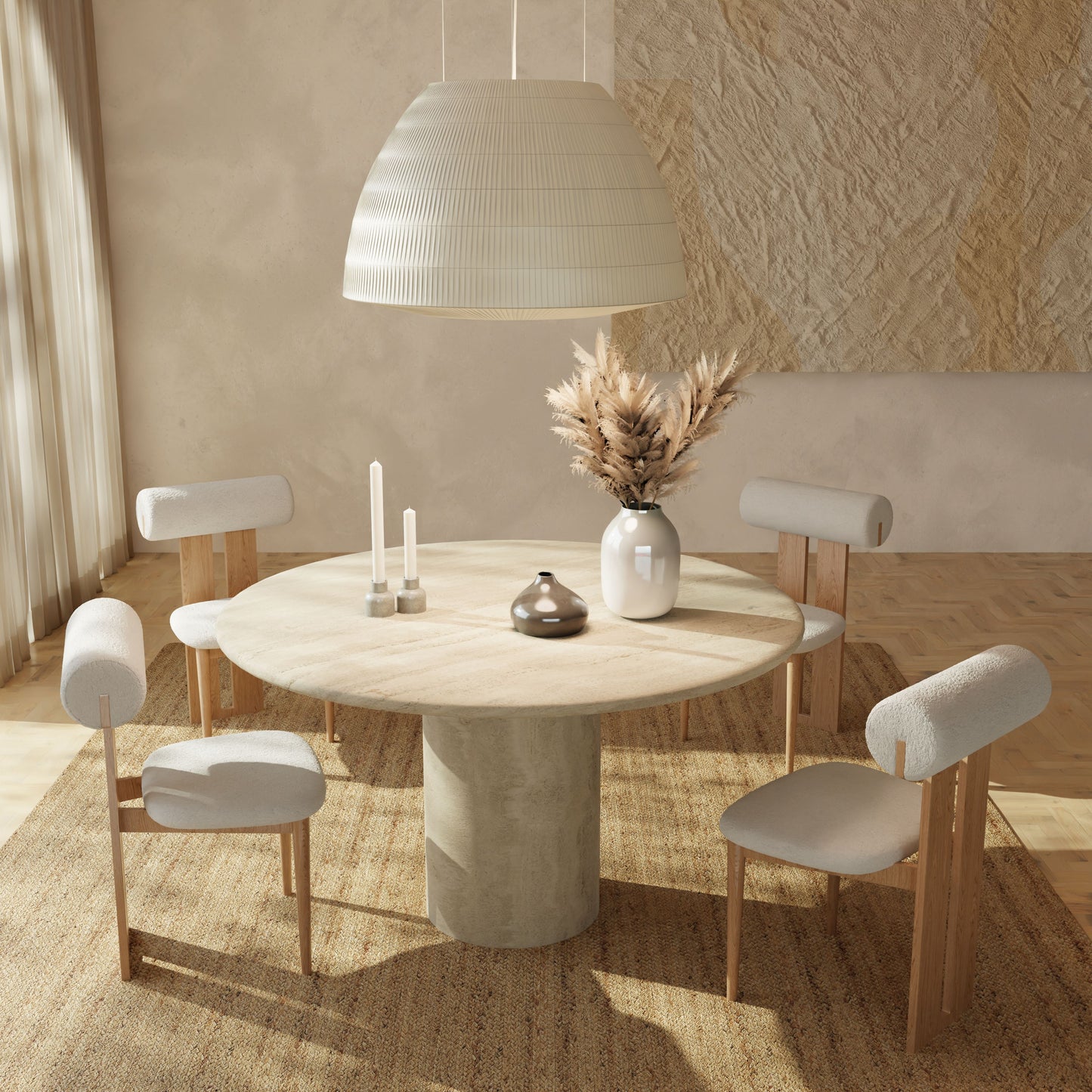 A minimalist dining room featuring the Renè + Templeton Dining Set—a round travertine pedestal table with four bouclé chairs—plus a large pendant lamp, candles, and a ceramic vase with pampas grass. Sunlight from the left highlights the neutral decor.
