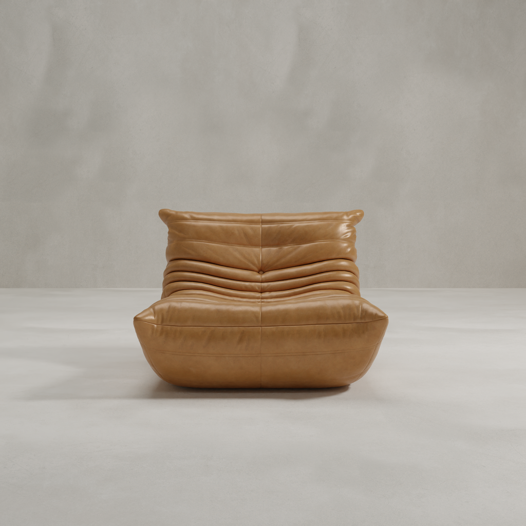 The Rolo Lounge Chair is a modern, tan leather 70s-inspired seat with a low profile, plush ruched cushions, and soft rounded edges, shown against a plain light grey background.