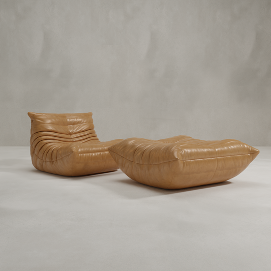 The Rolo Lounge Sofa Chair with Ottoman, featuring soft tufted tan leather and 70s-inspired design, sits on a smooth light floor against a plain gray wall.