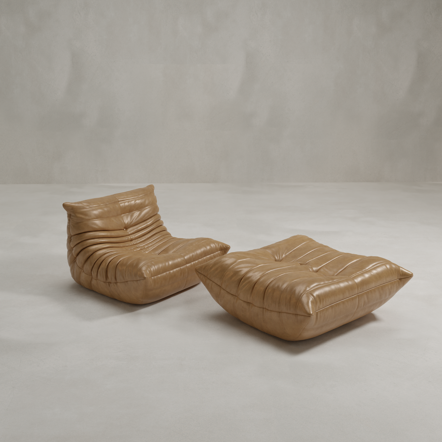 The Rolo Lounge Sofa Chair with Ottoman features a modern 70s-inspired design in tan leather, with plush, low-profile tufted cushions, set on a smooth light gray floor against a plain light gray wall.