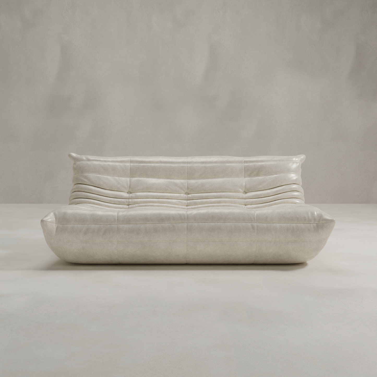 The Rolo Lounge Three Seater is a modern, low-profile beige leather sofa with tufted cushions and curved lines, set against a neutral wall and floor for a timeless mid-century look.