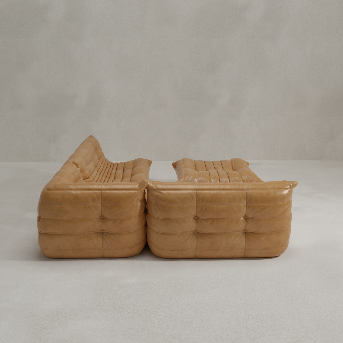 Two Rolo Lounge Four Piece Sofas in tan leather with tufted cushions, inspired by mid-century design, are arranged facing each other in a minimalist room with a light gray floor and plain light walls.