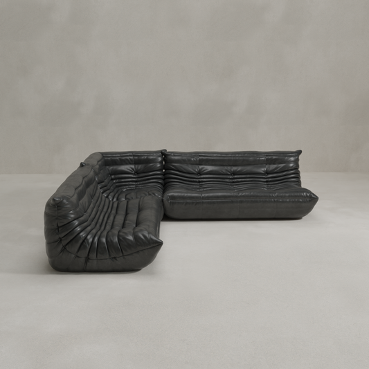 The Rolo Lounge Three Piece Sofa, a modern black leather sectional with deep tufting and wide, low seats, sits on a light grey floor against a plain light grey wall, reflecting modular system design.