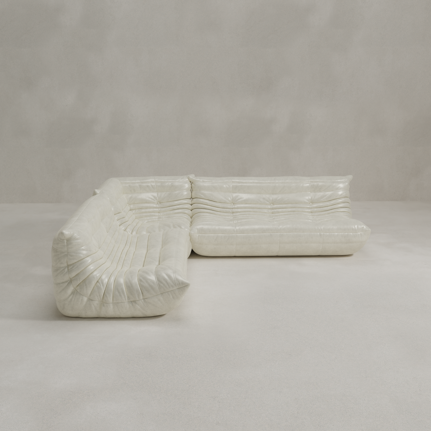 The Rolo Lounge Three Piece Sofa, a modern white tufted sectional with a low cushioned profile and modular design, sits in a minimal light-colored room with smooth floors and plain walls.