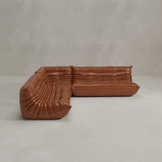 The Rolo Lounge Three Piece Sofa features brown leather upholstery, deep button tufting, and a low modern silhouette that recalls mid-century design, displayed against a plain light gray wall and floor.