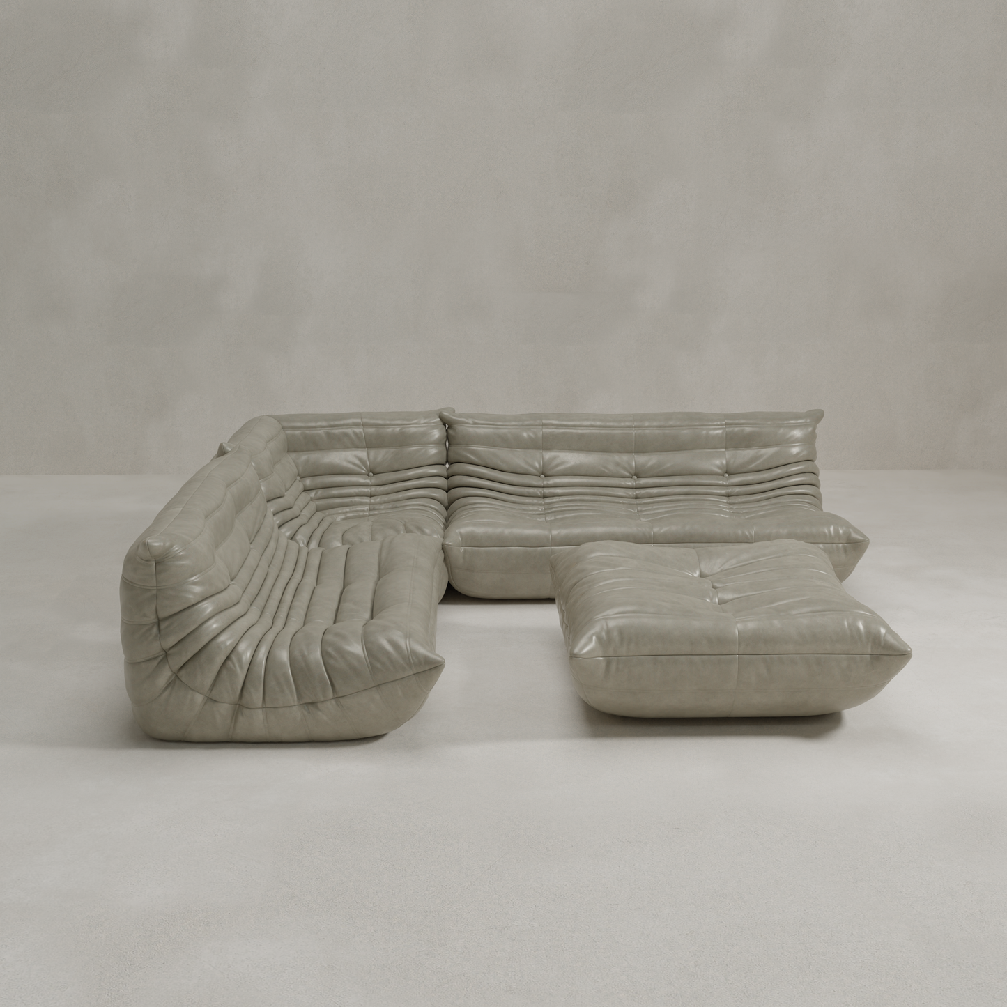 The Rolo Lounge Four Piece Sofa is a modern, light gray leather sectional with deep cushions and tufted details, featuring a modular design set on a smooth, light floor against a plain textured wall.