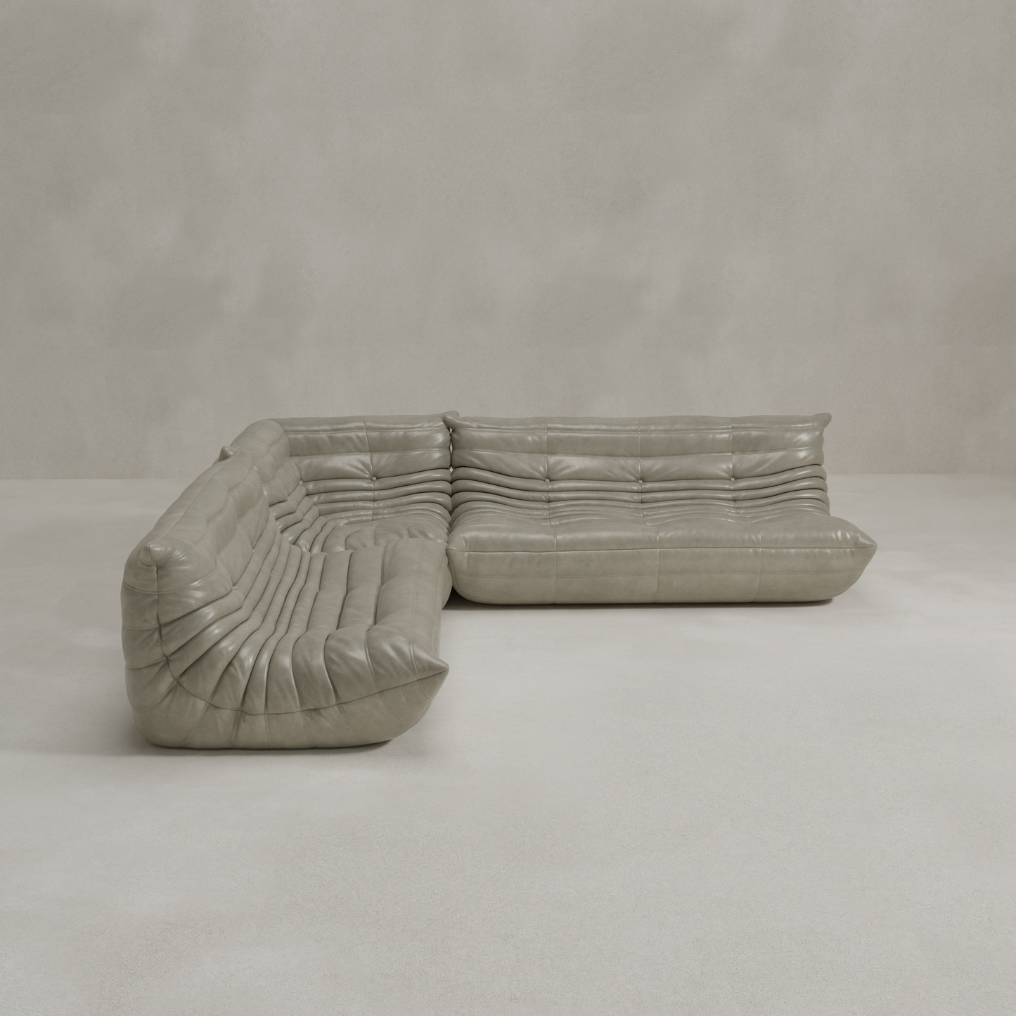 The Rolo Lounge Three Piece Sofa, an L-shaped sectional with tufted light gray leather upholstery and mid-century design, sits in an empty room with matching light gray walls and floor.