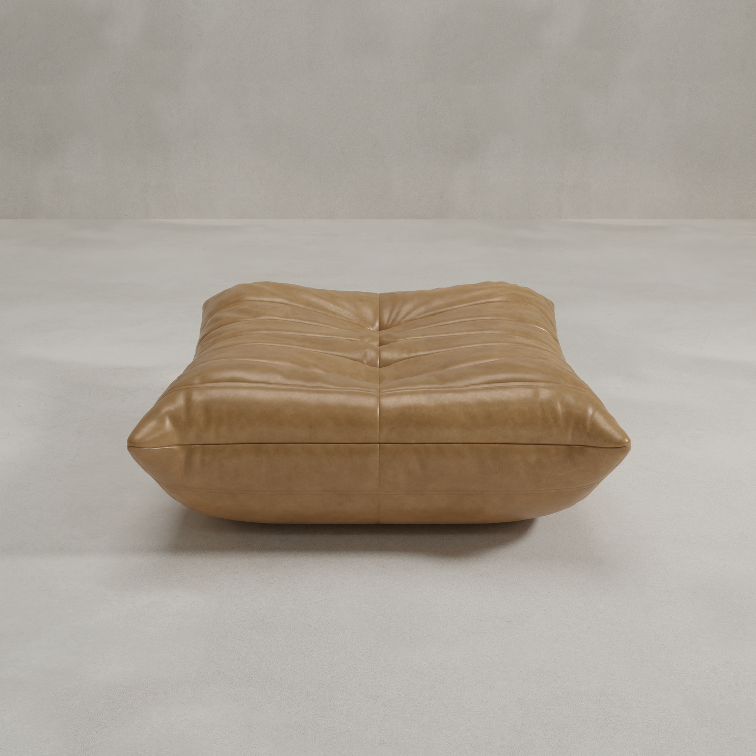 The Rolo Ottoman is a large tan leather floor cushion with tufted details and a soft, padded look, ideal as an ottoman or extra seat. It rests on a smooth light gray surface with a plain, light background.