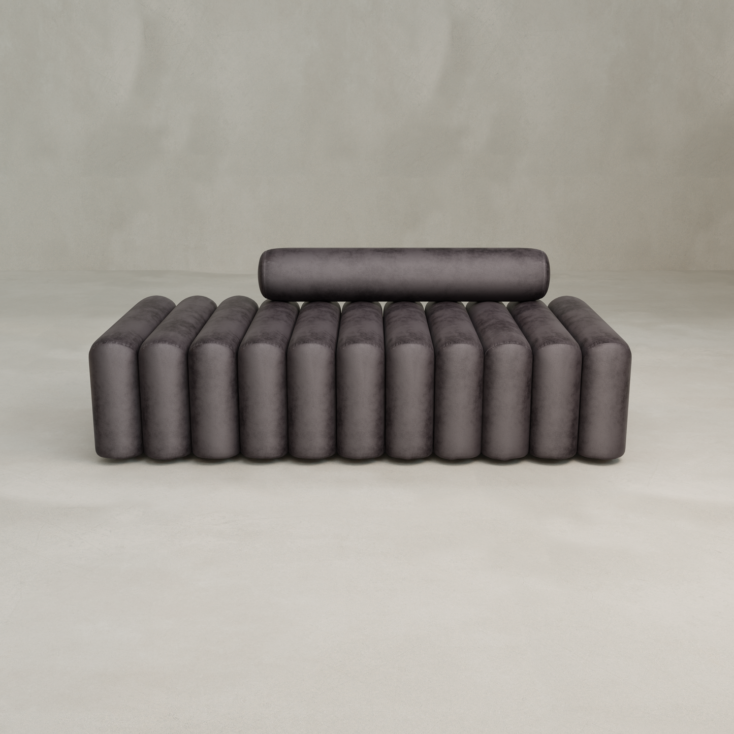 The Sonorra Bench Large features a modern minimalist design with quilted dark gray velvet and vertical cylindrical cushions, complemented by a matching cylindrical backrest, set against a plain light gray background.