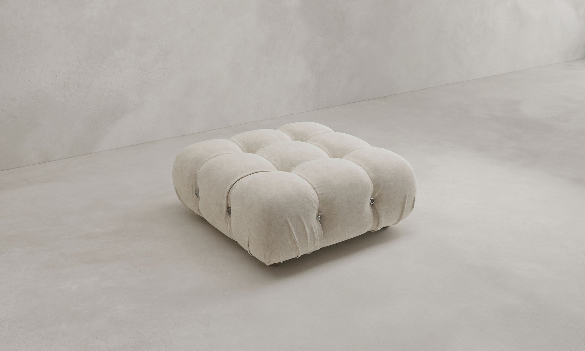 The Belmont Ottoman, a square, tufted piece upholstered in light beige fabric with refined button detailing and classic style, is set against a plain light gray background.