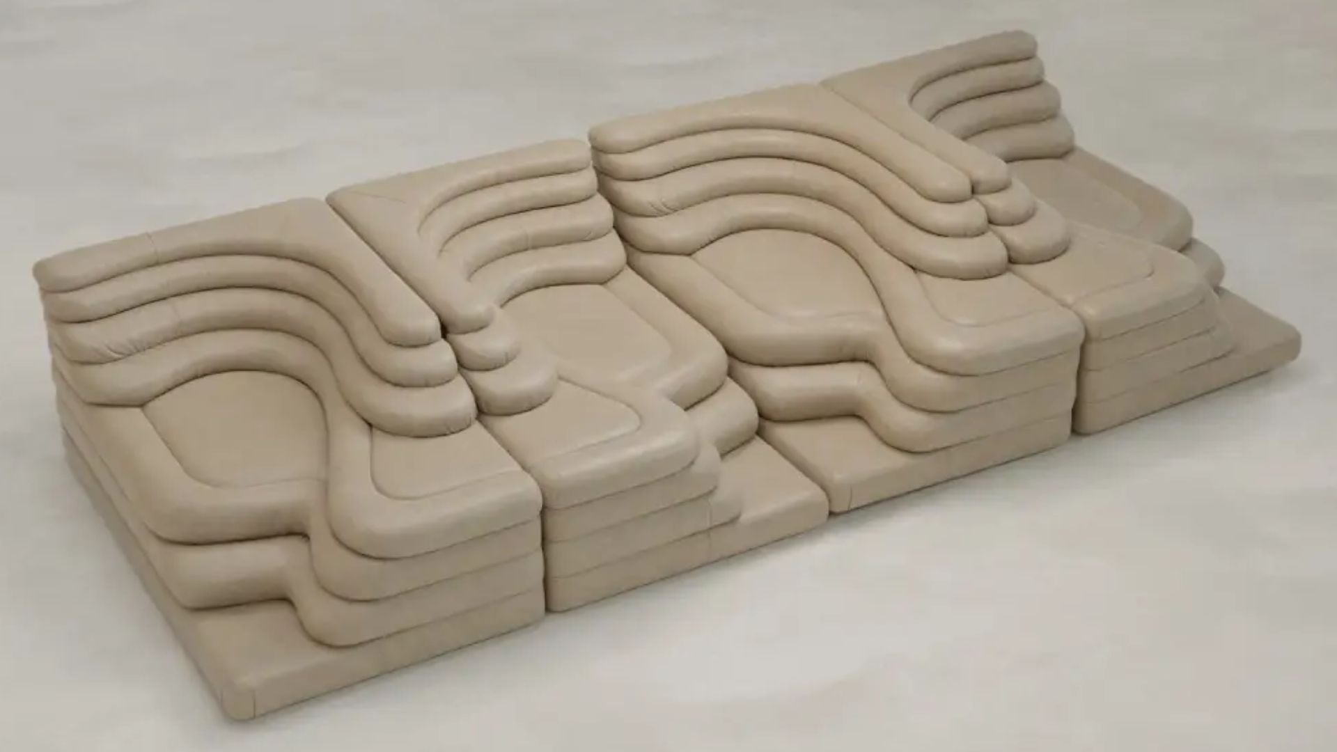 The Cascata 4 Piece Sofa Rental features sculpted, wave-like cushions and a modular beige design, adding luxurious style to any light, neutral floor.